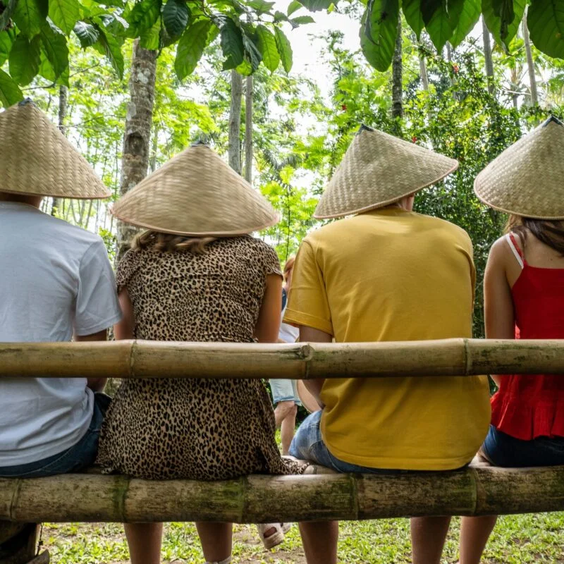people wearing asian conical hats while sitting on a bamboo bench